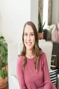 Woman smiling while seated on a white couch in a cozy living room.