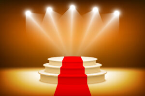 An illuminated stage with spotlights and a red carpet leading to a circular podium on an amber background.